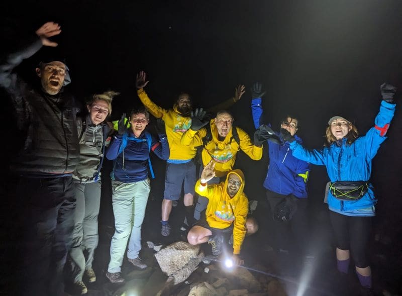 A group of trekkers celebrating at the top of a mountain at night.