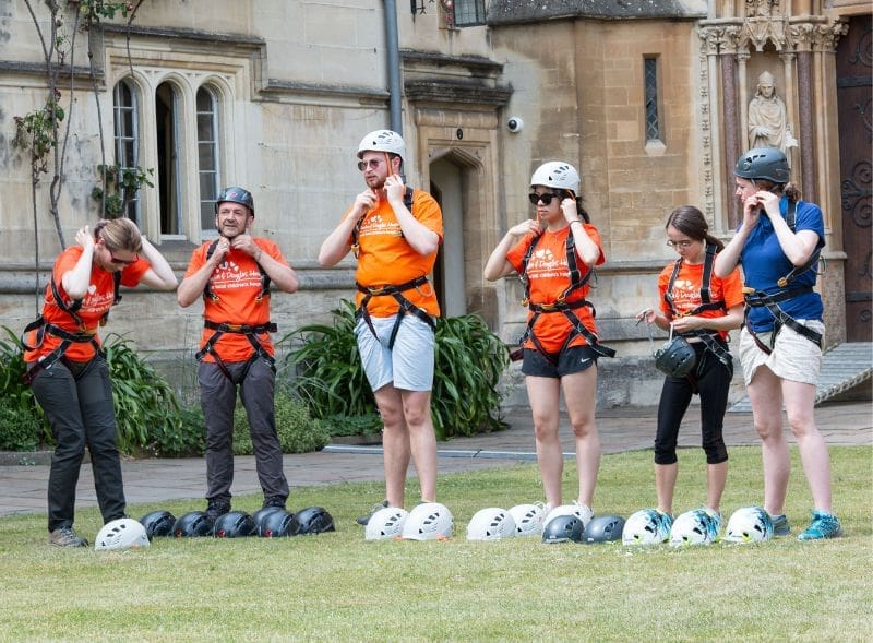 Six people putting on helmets and harnesses, ready to take part in an abseil.
