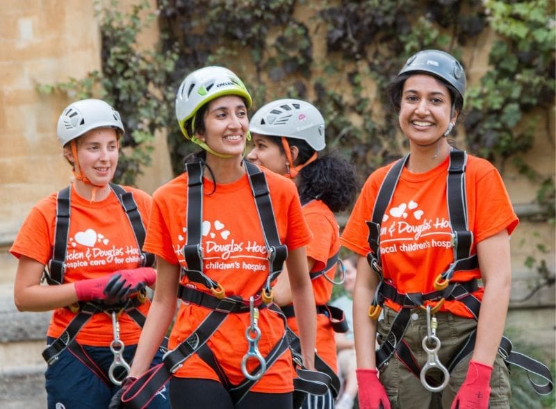 Four young women wearing helmets and harnesses, ready to take part in an abseil challenge.