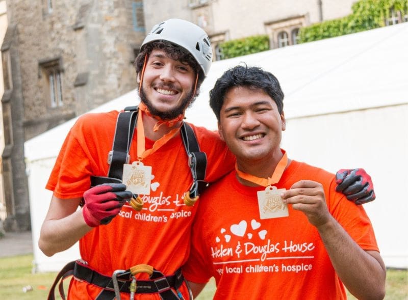 Two men smiling and holding up their Abseil completion medals