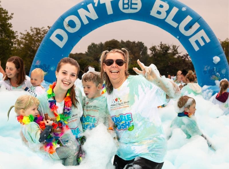 Two smiling women with two young children are surrounded by blue bubbles.