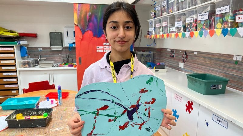 Ayeza, a care team volunteer at Helen & Douglas House hospice, is holding up a marble art painting. 